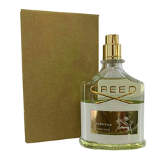 Product shot of a Creed Aventus For Her perfume bottle featuring a clear glass body with gold "CREED" lettering and cap, a white label displaying the iconic horse and rider silhouette, and light green liquid, standing beside a plain brown box
