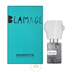 Nasomatto Blamage perfume product photography showing a vibrant teal box with black handwritten "BLAMAGE" text alongside its bottle featuring a distressed black and white wood grain texture and an irregular white crumpled cap
