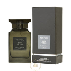Tom Ford's Oud Wood fragrance features a dark olive green rectangular glass bottle with a wide black cap next to its tall, textured dark gray box, both prominently displaying the iconic Tom Ford Oud Wood 100 ML branding