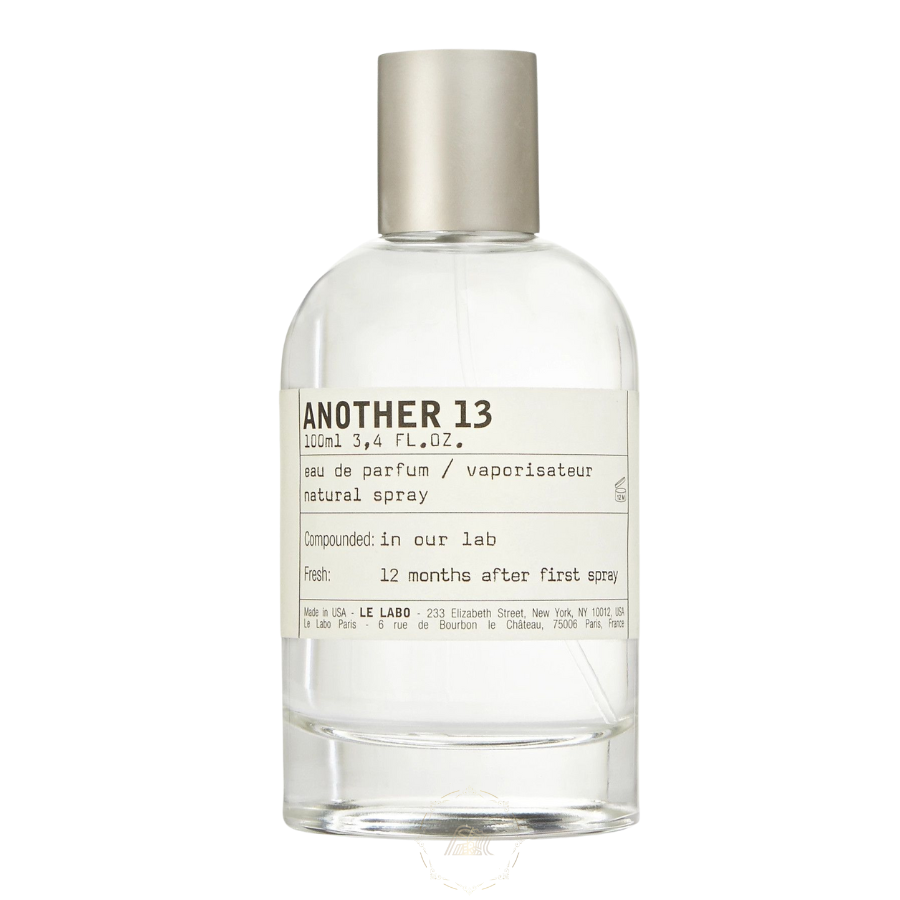 Product photo of Le Labo Another 13 Eau de Parfum, a minimalist 100ml clear glass bottle with a brushed silver cap and white label detailing its New York and Paris origins, with text 'Compounded in our lab' and '12 months after first spray'