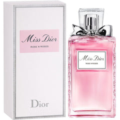 Product photography featuring a Miss Dior Rose N'Roses perfume bottle with pink liquid, a silver bow, and textured glass sides beside its matching white box with a pink label