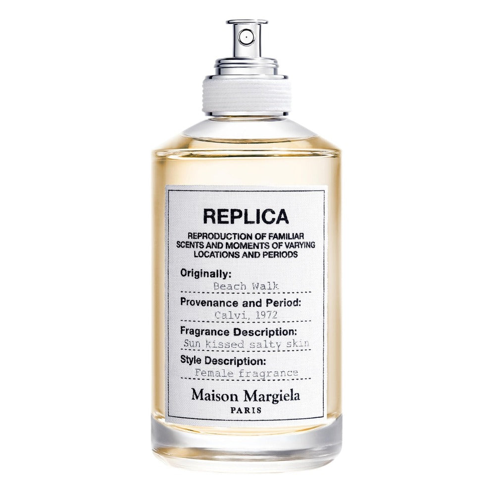 Maison Margiela Replica Beach Walk perfume bottle, a clear glass rectangular container with light amber liquid, features a distinctive white fabric label detailing its Calvi 1972 provenance and "Sun kissed salty skin" fragrance description