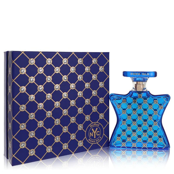 Photograph of Bond No. 9 NoMad NYC fragrance featuring a deep blue hourglass-shaped bottle and its matching box, both adorned with an intricate gold lattice pattern and sparkling crystal-like embellishments