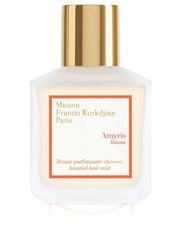 Product photography by Maison Francis Kurkdjian of a frosted glass bottle of Amyris Femme scented hair mist from Paris featuring a gleaming gold cap and an orange-bordered white label