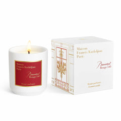 Product photograph of a Maison Francis Kurkdjian Paris Baccarat Rouge 540 scented candle, a lit white ceramic candle with a red label, next to its white box displaying a gold and red chandelier window design evoking Parisian grandeur