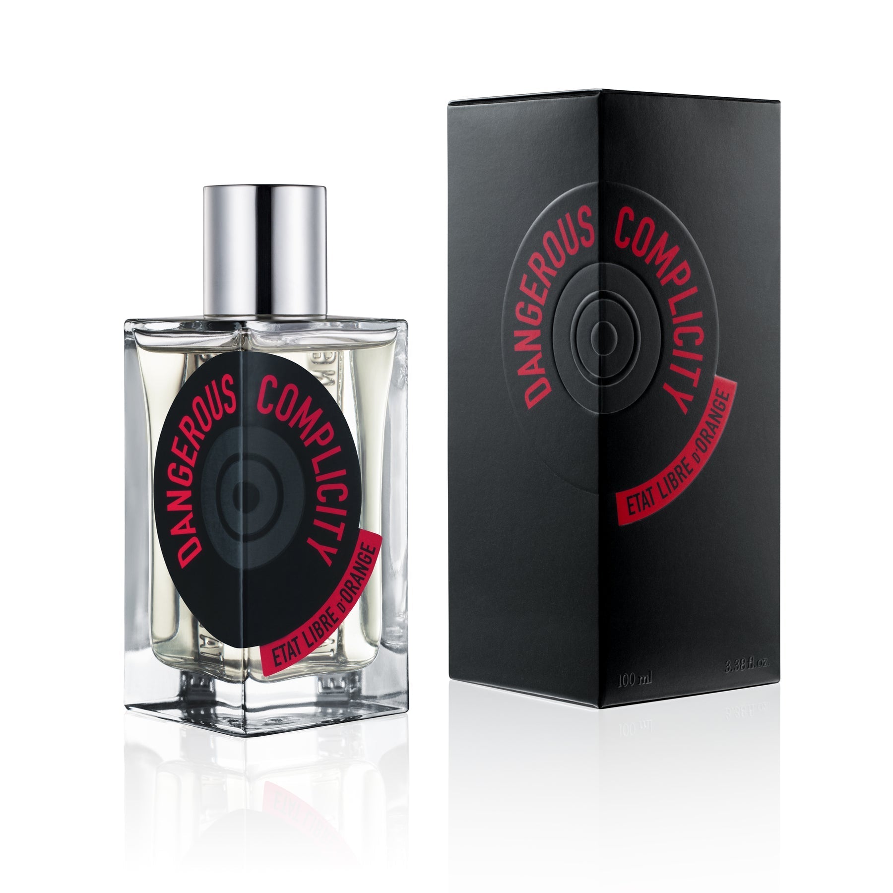 Product photography by Etat Libre d'Orange featuring the Dangerous Complicity fragrance in a clear glass bottle with a silver cap and a black circular label with red text, alongside its matching black embossed box, all on a white reflective surface