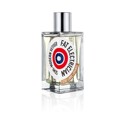 A clear rectangular glass perfume bottle with a shiny silver cap, a white circular label displaying "FAT ELECTRICIAN SEMI-MODERN VETIVER" in black text around a red and blue target, and a brown "ETAT LIBRE D'ORANGE" label at its base, on a white reflective surface