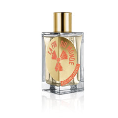 Digital photograph by Etat Libre d'Orange of their La Fin Du Monde perfume bottle, a clear glass rectangular bottle with a gold cap and a unique gold circular label featuring distressed red 'LA FIN DU MONDE' text, an orange mushroom cloud graphic, and a red brand banner