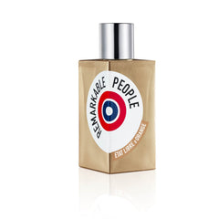 Photograph by Etat Libre d'Orange of their Remarkable People perfume bottle, a golden-brown rectangular bottle with a silver cap and a white circular label displaying the product name, a red white and blue target logo, and Etat Libre d'Orange branding on a brown banner against a white studio background