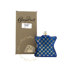 A product image of a Bond No 9 New York NoMad Tester perfume featuring a distinctive deep royal blue bottle with a gold lattice pattern and crystal accents standing beside its natural kraft brown box marked with the brand name and product details