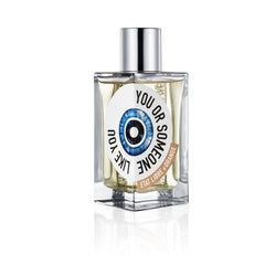 Digital photography of the Etat Libre d'Orange You or Someone Like You perfume bottle on a white studio background, showcasing its square clear glass, shiny silver cap, and a distinctive circular label with a vibrant blue eye design and a brown banner