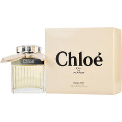 Product photography by Chloe features a ribbed clear glass bottle of Chloe Eau de Parfum with light amber liquid, a silver cap, and a beige ribbon, alongside its matching beige box prominently displaying the black Chloé logo and 2.5 FL.OZ e 75 ml volume