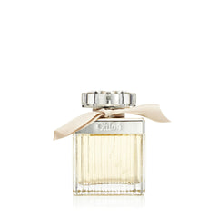 Chloe perfume bottle a clear rectangular fluted glass bottle with light yellow liquid a silver neck band engraved with Chloé a decorative scalloped clear cap and a beige ribbon tied elegantly around its neck