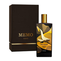 Product photo by MEMO PARIS of an Ocean Leather Eau de Parfum bottle and dark brown box from Paris displaying a white whale illustration over gold and black geometric patterns with gold branding