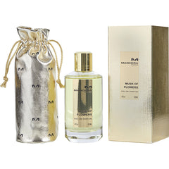 Product photography by Mancera Paris featuring a clear glass bottle of Musk of Flowers Eau de Parfum, a gold metallic drawstring pouch with M logos, and a gold textured gift box