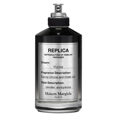 Maison Margiela Replica fragrance bottle, a dark opaque vessel with a silver label featuring REPLICA branding, the dream Flying, and a fragrance description Fusing citrus and fresh air gender anonymous