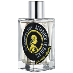 Etat Libre d'Orange perfume bottle, a clear rectangular glass bottle with a shiny silver cap and a prominent black and yellow circular label featuring a profile portrait of Marquis de Sade and the text Attaquer le Soleil Etat Libre d'Orange