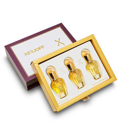 Xerjoff perfume gift set featuring a deep purple and white box with gold branding and three small clear bottles of Naxos, Alexandria II, and Golden Dallah fragrances with elegant golden caps in a gold presentation tray